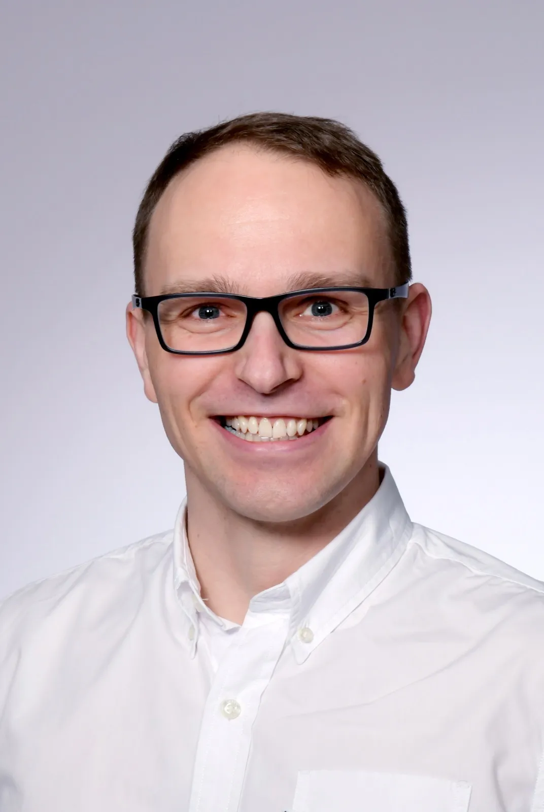 Manuel Villmer in a white shirt, smiling, against a light gray background